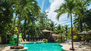 A swimming pool surrounded by palm trees and lounge chairs, with a building in the background. - Large Bungalow in Banana Beach, with King and Queen Bed. A/C, Wifi, Kitchenette (Santa Teresa Costa Rica)