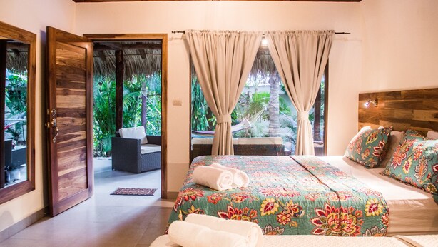 A bedroom with a bed, curtains, and a view of a garden. - Large Bungalow in Banana Beach, with King and Queen Bed. A/C, Wifi, Kitchenette (Santa Teresa Costa Rica)