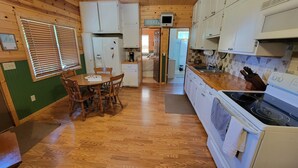 A compact kitchen with wooden cabinets, a dining table with chairs, a refrigerator, a stove, and a sink.