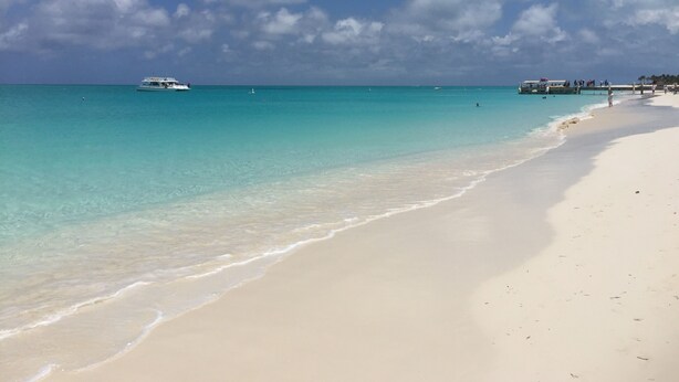 Ein Strand mit klarem türkisblauem Wasser, einem weißen Sandstrand und einem Boot in der Ferne.