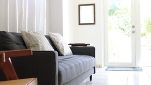 Ein modernes Wohnzimmer mit einem grauen Sofa, gemusterten Kissen, einem Holztisch und einer Tür zu einem Garten.