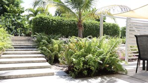 Ein Garten mit einer Betonstiege, einer Palme und einem weißen Pergola mit einem Stuhl.