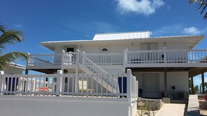 Un edificio de dos pisos con fachada blanca, un balcón en el nivel superior y una escalera que conduce a la entrada.