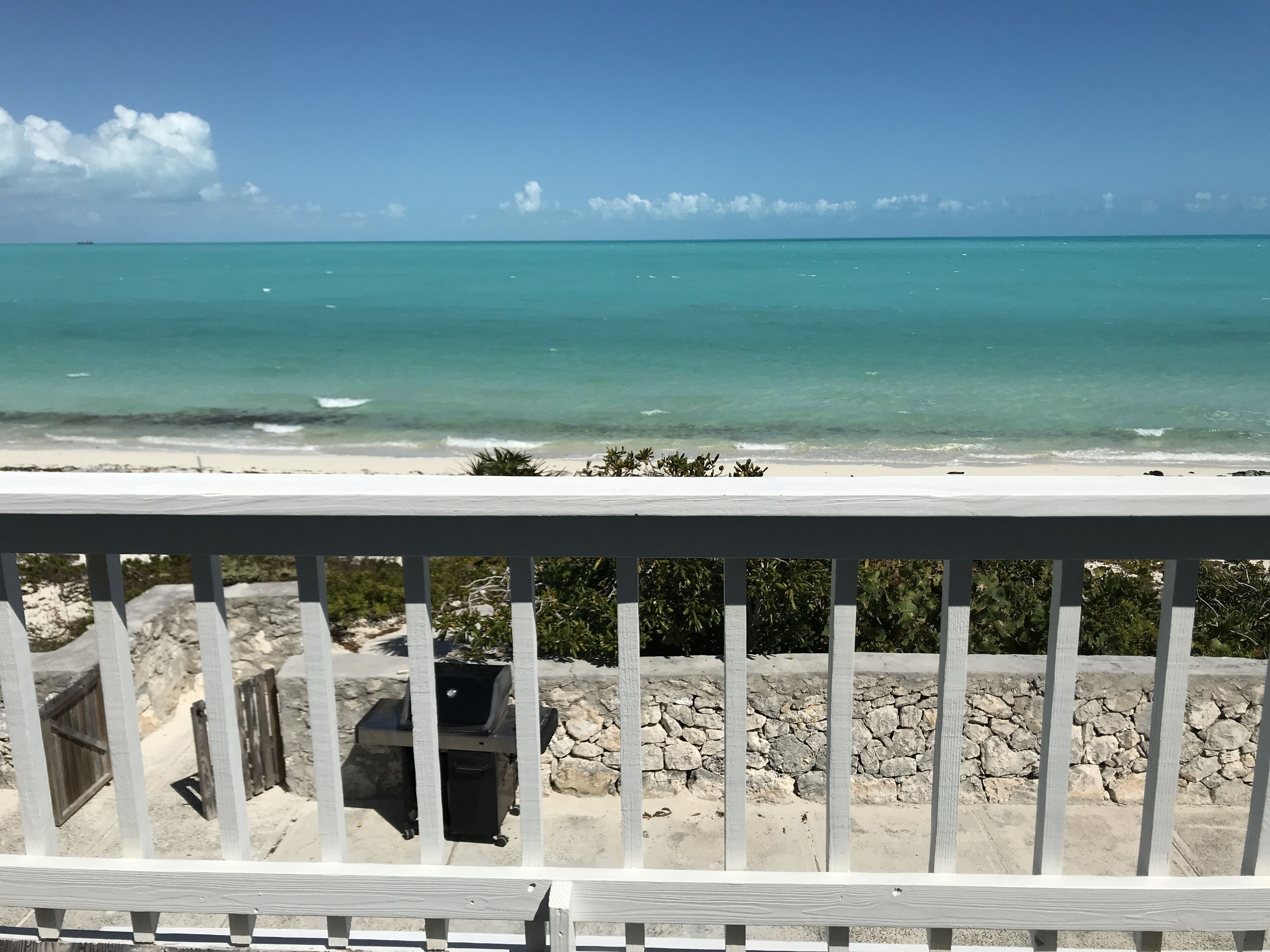 A beach view from a balcony with a stone wall and a grill.