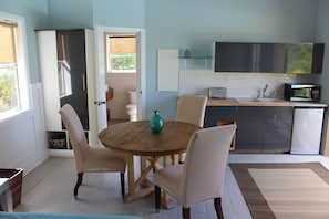 Een kleine keuken met een ronde houten tafel, witte stoelen, een smaragdgroene vaas en een magnetron.