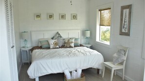 A bedroom with a bed, bedside tables, a chair, a window, and wall-mounted artwork.