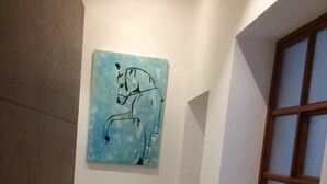 A hallway with a checkered floor, a wall-mounted artwork of a horse, and a window with a wooden frame.