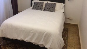 A neatly made bed with patterned pillows, a wall-mounted branch mural, and a hanging light fixture.