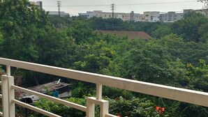 Varanda com guarda-corpo metálico, vista para uma área verde exuberante com árvores e um edifício ao fundo.