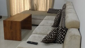 Uma sala de estar com um sofá, uma mesa de centro de madeira e um controle remoto sobre o sofá.