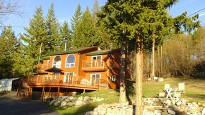 A wooden cabin with a balcony, surrounded by trees and a stone wall. - Quiet Peaceful Carmi Mountain Home. (Penticton)