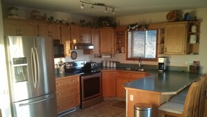 A kitchen with wooden cabinets, a stainless steel refrigerator, a stove, and a sink. - Quiet Peaceful Carmi Mountain Home. (Penticton)