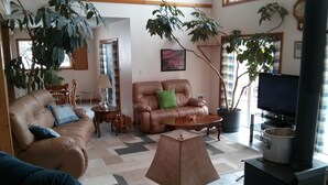 A living room with a sofa, armchair, coffee table, and a TV. There are potted plants and a fireplace. - Quiet Peaceful Carmi Mountain Home. (Penticton)