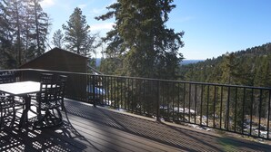 En træterrasse med et bord og stole, med udsigt over et skovområde og en hytte.
