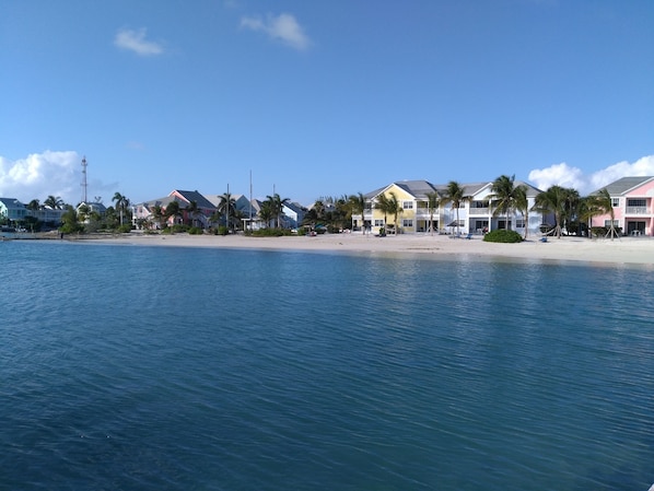 Une propriété située en bord de mer, avec plusieurs bâtiments aux couleurs vives, une plage de sable et des palmiers.