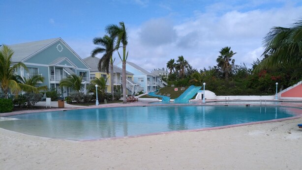 A resort pool with a water slide, palm trees, and a beach area.