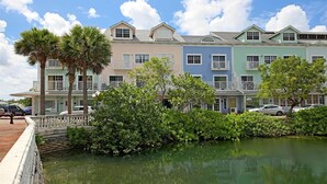 A row of colorful townhouses with balconies, a small bridge, and a calm water body in the foreground.