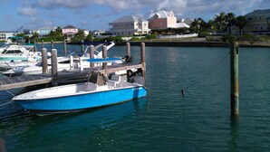 A marina with boats docked, a wooden pier, and houses in the background.