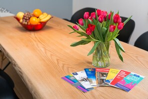Une table en bois ornée d’un vase de tulipes rouges, d’un saladier de fruits et de quelques brochures.