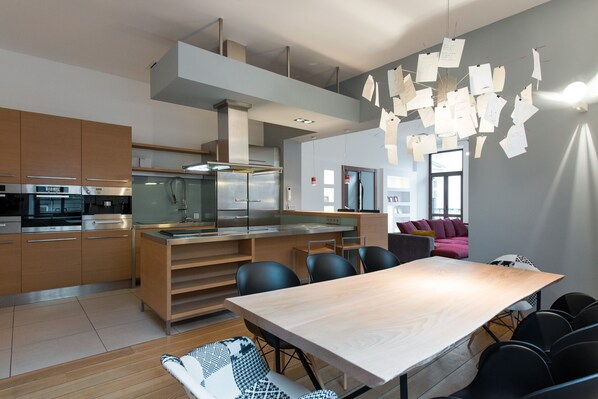 Une cuisine moderne équipée d’appareils électroménagers en acier inoxydable, une table à manger en bois et un coin salon avec un canapé et des fauteuils.