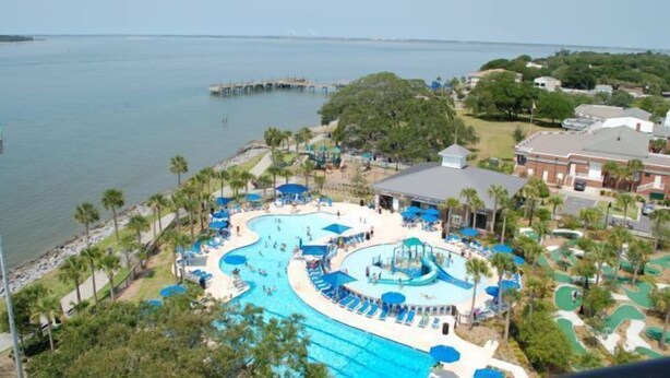 Un resort con una piscina grande, palmeras y un muelle que se adentra en el agua.