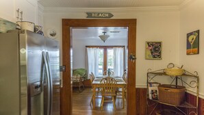 Una cocina con refrigerador de acero inoxidable, mesa y sillas de madera. Un letrero sobre la puerta dice "BEACH".