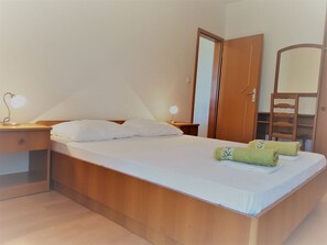 A neatly made bed with white linens, two bedside lamps, a wooden nightstand, a wooden wardrobe, and a mirror.