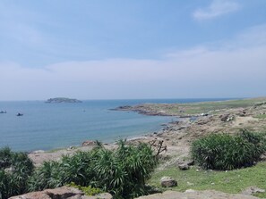 Un paysage côtier caractérisé par un terrain rocheux, une végétation clairsemée et une île visible au loin.
