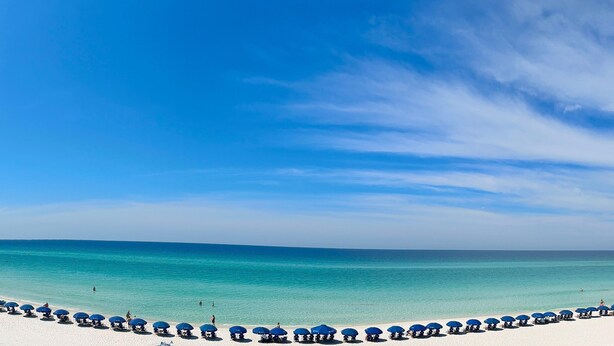 Une plage bordée de rangées de parasols bleus et de sable blanc.
