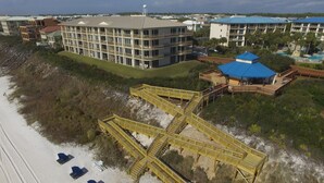 Un hôtel situé en bord de mer, avec une promenade jaune bien visible qui mène à la plage, entouré d’une végétation luxuriante et d’un grand bâtiment doté de nombreux balcons.