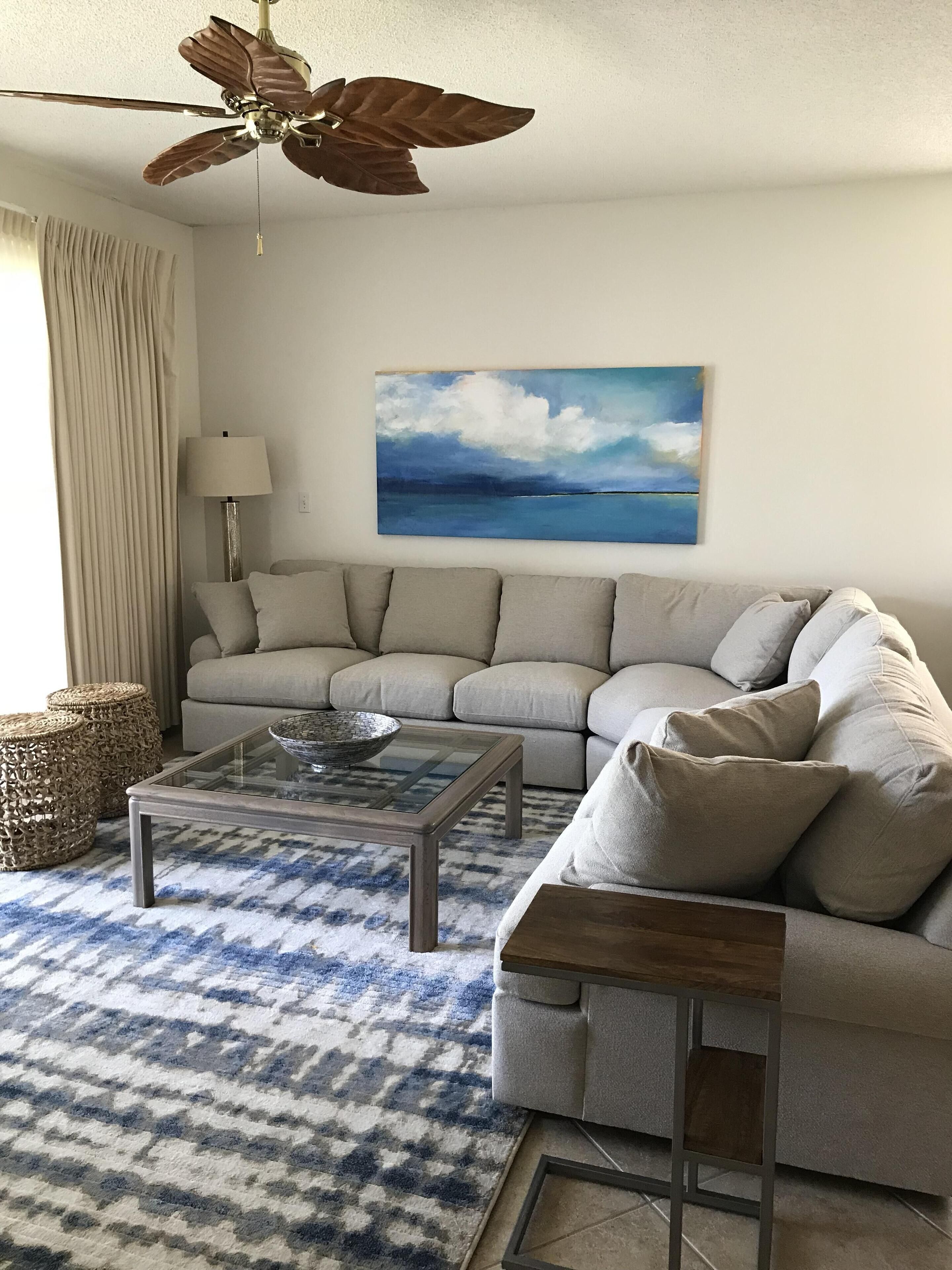 Ein Wohnzimmer mit einer Couch, einem Glastisch, einem Deckenventilator, einer Lampe, einem Bild und einem gemusterten Teppich.