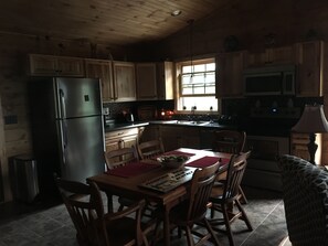 A cozy cabin-style kitchen with wooden cabinets, a refrigerator, a dining table with chairs, and a window providing natural light. - ENJOY A QUIET GETAWAY AT MOUNTAIN VIEW CABIN RENTALS (New Market)