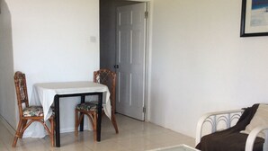 Una sala de estar con una mesa de centro de vidrio, un sofá, una mesa de comedor con sillas y una puerta al fondo.