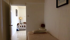 Un dormitorio con cama, mesita de noche, lámpara y puerta que da a otra habitación.