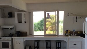 Una cocina con encimera blanca, dos taburetes, una estufa y una ventana con vistas a zonas verdes.