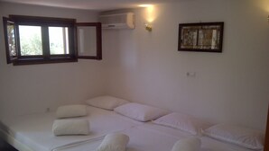 A bedroom with a bed, pillows, a window, an air conditioner, and a wall-mounted light fixture.
