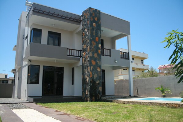 A modern two-story house with a central stone pillar, a balcony, and a swimming pool in the backyard.