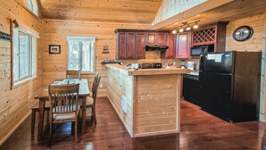 A wooden cabin interior with a dining area, kitchen, and a large window. - The Ridge At Glacier / Alpine Cabin #5 (Coram)