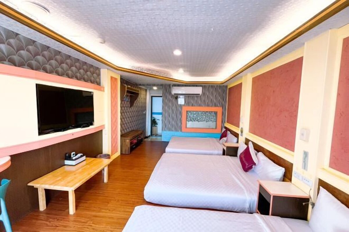 A hotel room with a TV, a desk, two beds, and a wall-mounted artwork.