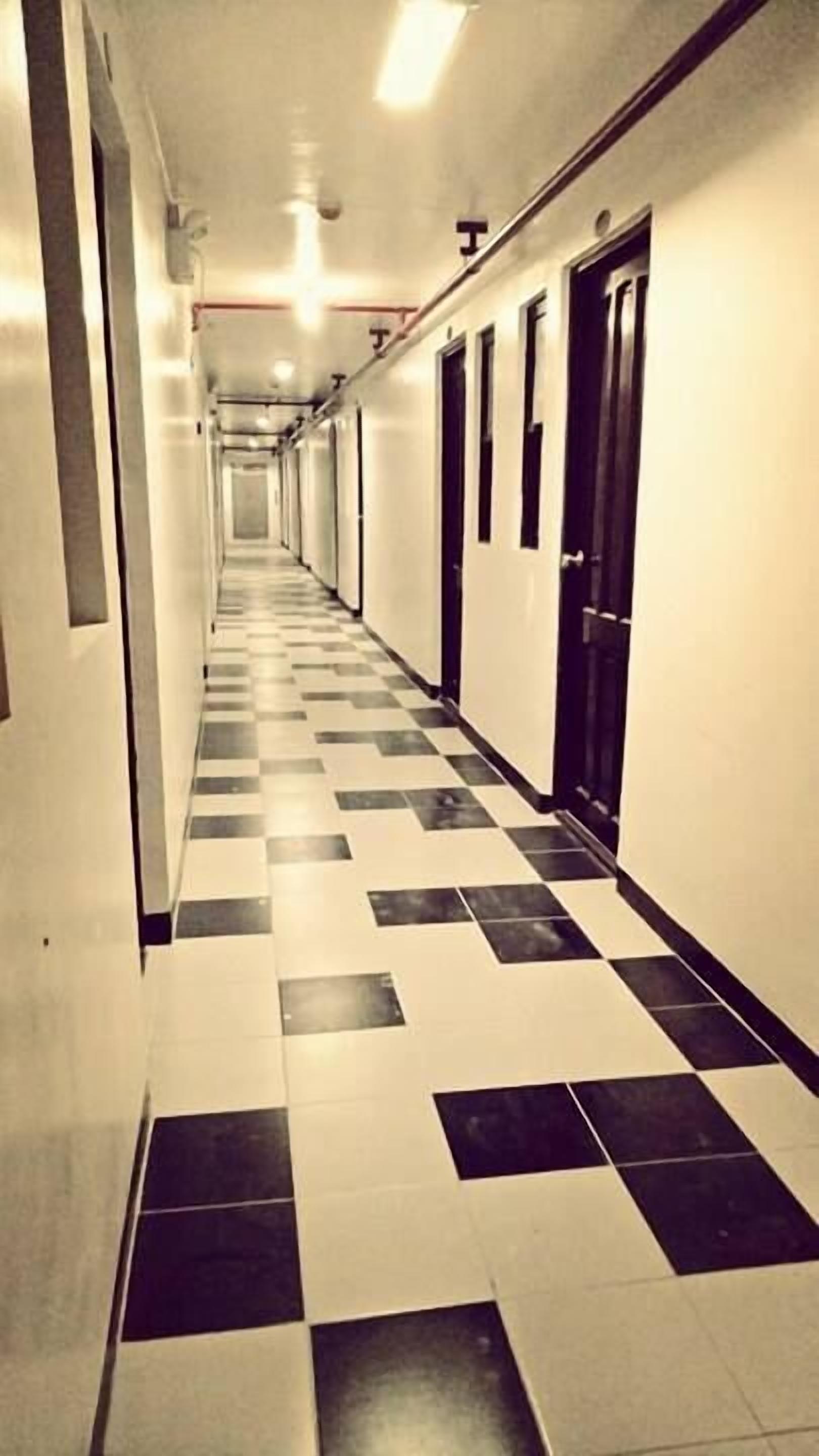Un pasillo largo y estrecho con suelo de cuadros, paredes blancas y puertas a un lado.