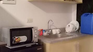 Una cocina compacta con microondas, un refrigerador pequeño, un lavamanos y un dispensador de agua azul.