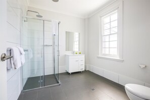 A modern bathroom with a glass-enclosed shower, a white vanity, and a large window providing natural light.