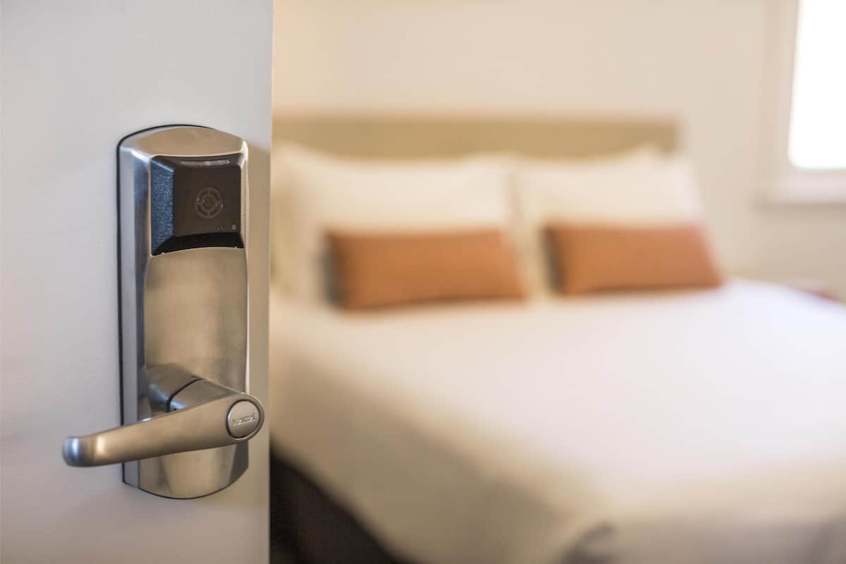 Una habitación de hotel moderna con un picaporte metálico, una cama bien hecha con dos almohadas y una ventana que proporciona luz natural.