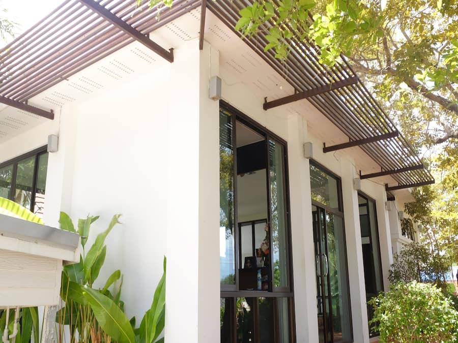 A modern building with large windows, a white exterior, and a wooden pergola.