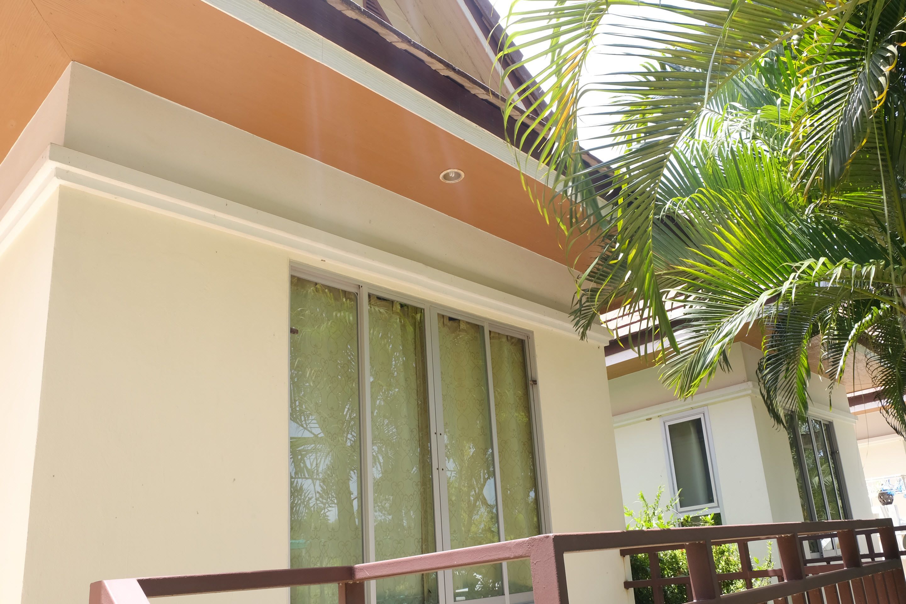 A building with a balcony, large windows, and a palm tree.