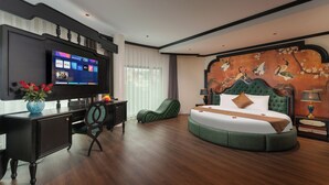 Ein modernes Hotelzimmer mit einem großen Flachbildfernseher, einem runden Bett, einem Schreibtisch mit Stuhl und einer dekorativen Wandmalerei.