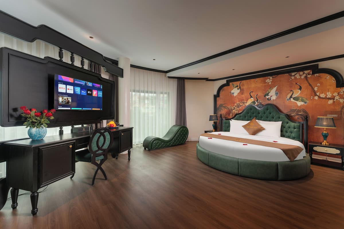 Una habitación de hotel moderna con una amplia televisión de pantalla plana, una cama redonda, un escritorio con una silla y un mural decorativo en la pared.