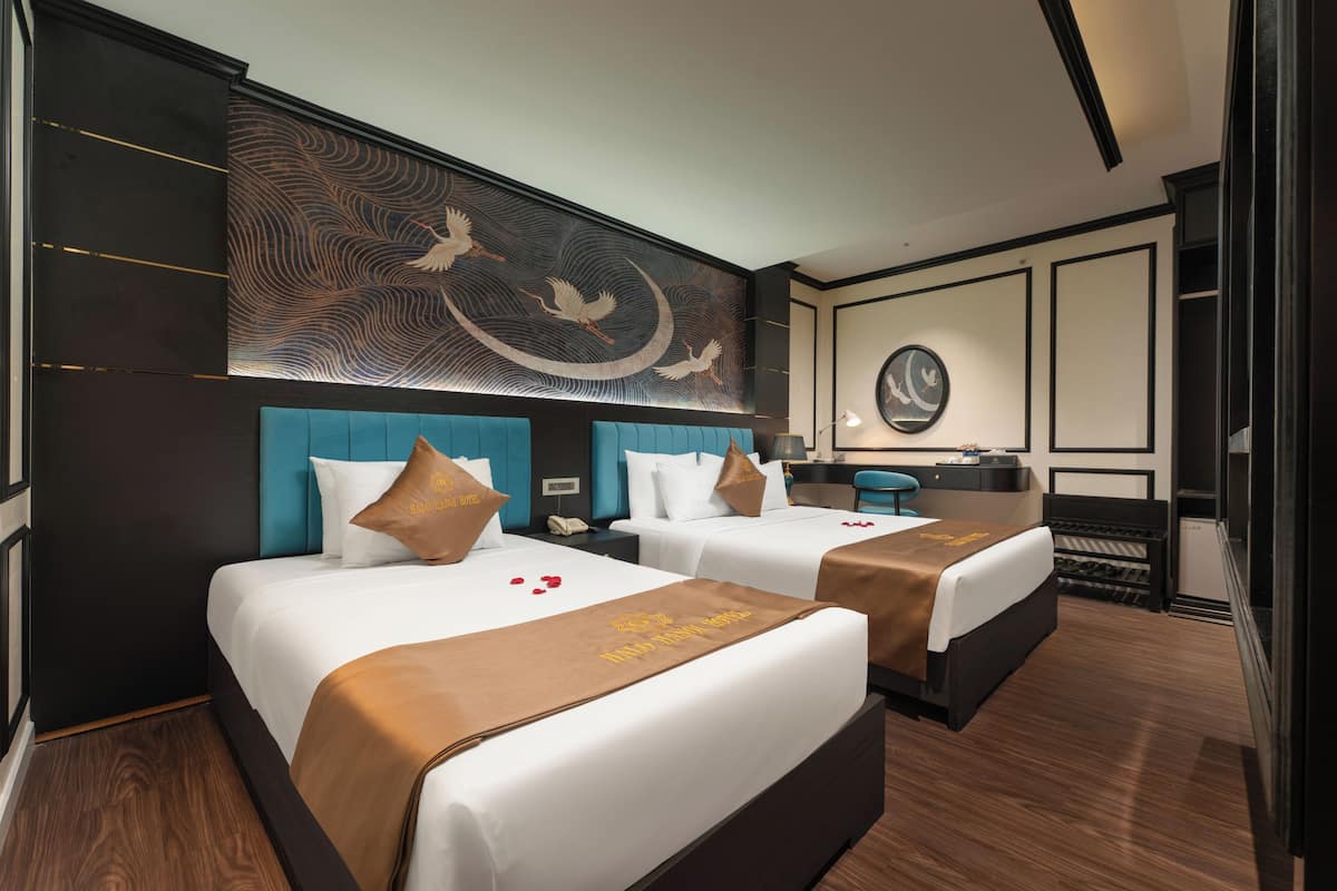 Habitación de hotel con dos camas, un mural grande en la pared, un espejo redondo y un escritorio con una silla.