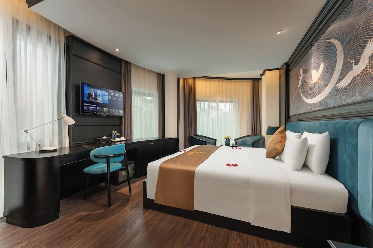Habitación de hotel con cama, escritorio, silla, televisor y una obra de arte en la pared.