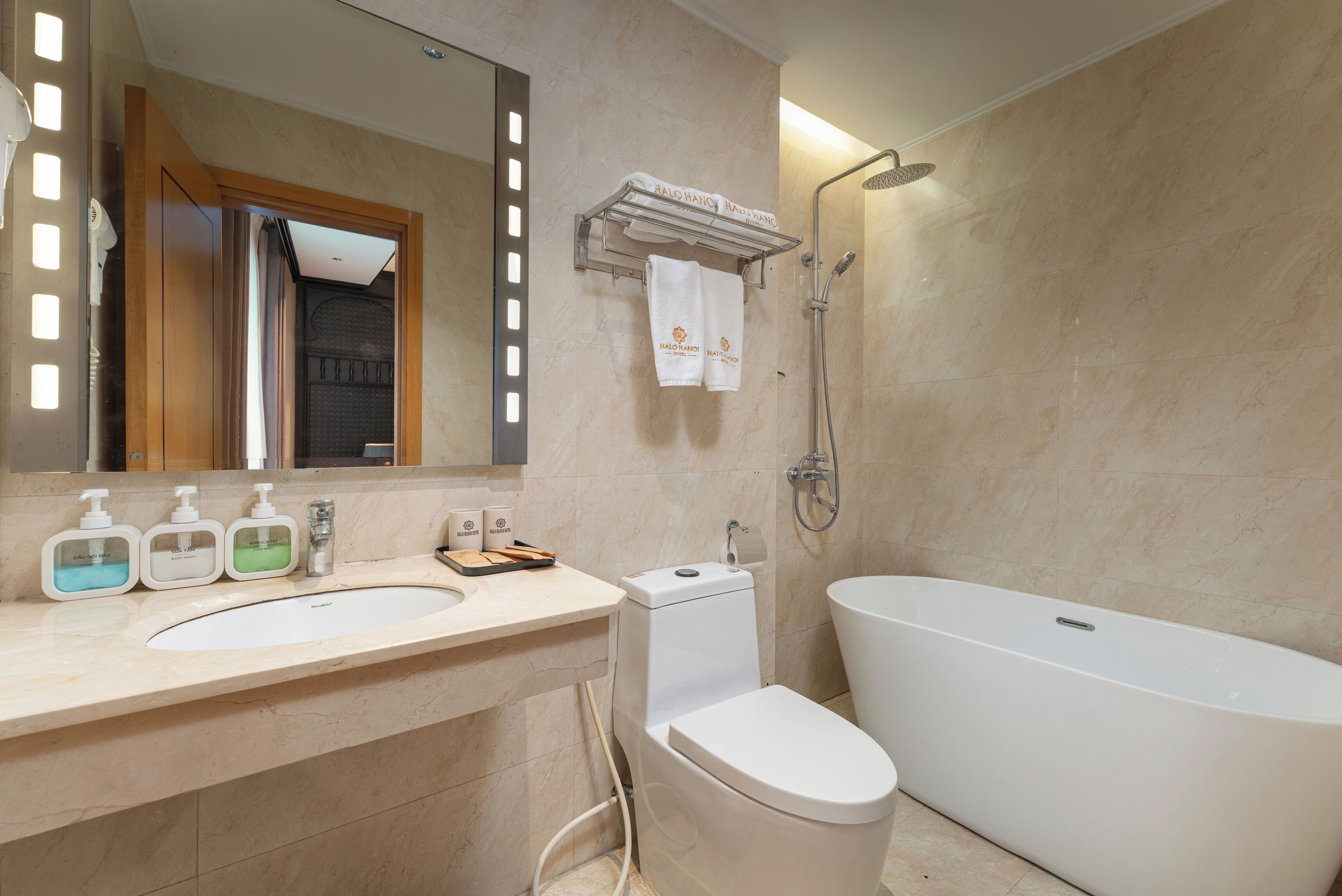 A modern bathroom with a large bathtub, a toilet, a sink with soap dispensers, and a towel rack with towels.